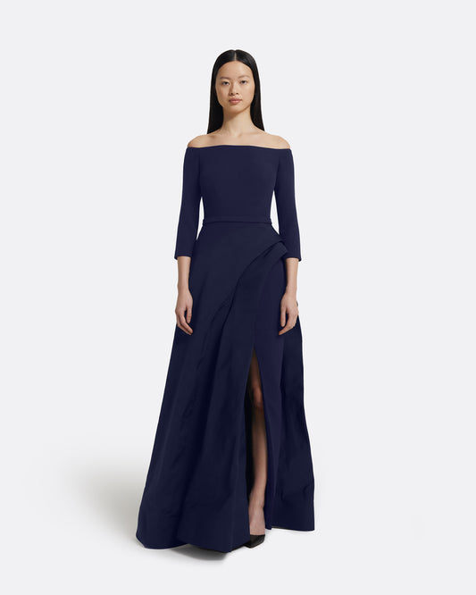 Woman wearing a navy off-shoulder gown with a slit on a white background